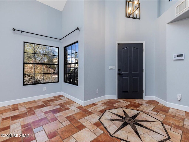 foyer with stone finish floor, baseboards, visible vents, and a towering ceiling