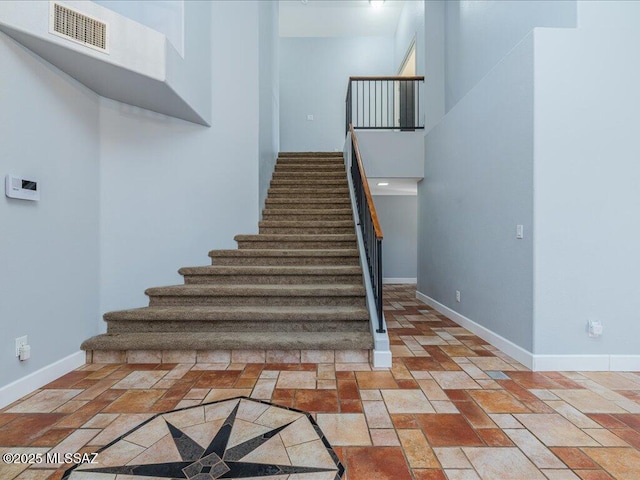 stairway with visible vents, baseboards, and a towering ceiling