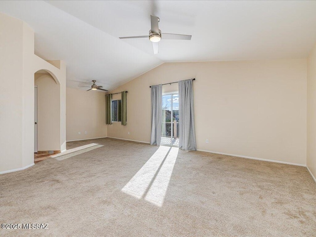 carpeted spare room with lofted ceiling, a ceiling fan, arched walkways, and baseboards