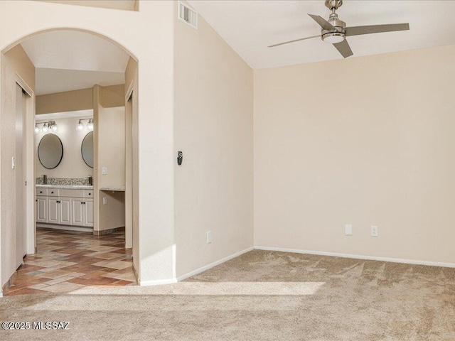 spare room featuring visible vents, baseboards, arched walkways, ceiling fan, and light colored carpet