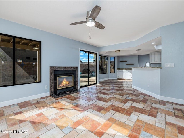 unfurnished living room featuring a tiled fireplace, a ceiling fan, and baseboards