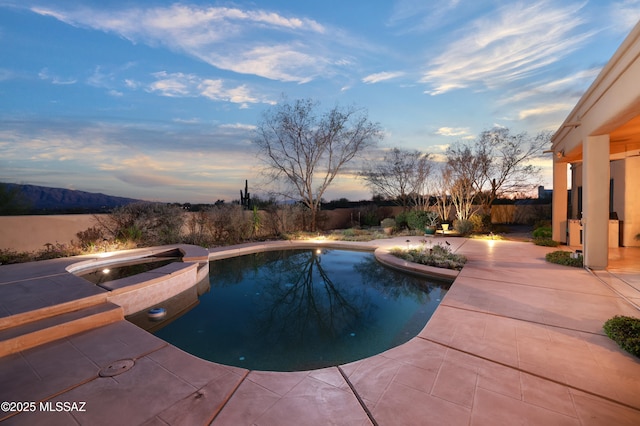 pool at dusk featuring a patio, fence, an in ground hot tub, and an outdoor pool