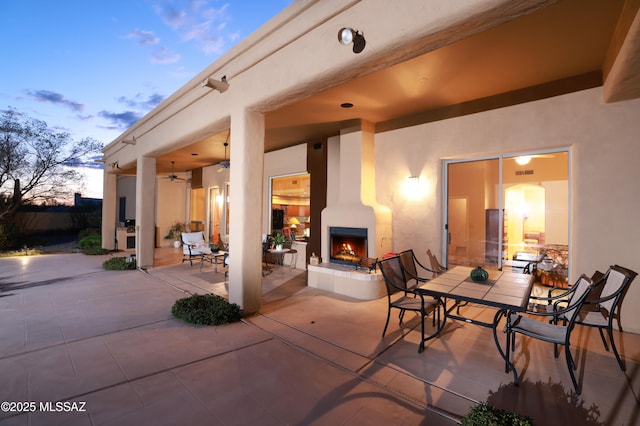 view of patio / terrace featuring outdoor dining space, visible vents, a lit fireplace, and ceiling fan