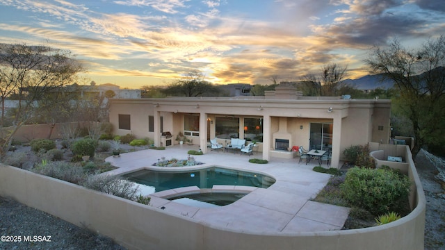 back of property at dusk with a patio area, stucco siding, an in ground hot tub, and fence