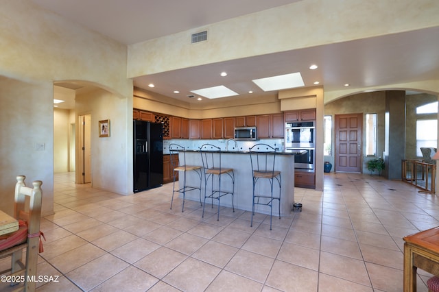 kitchen featuring visible vents, light tile patterned flooring, arched walkways, stainless steel appliances, and a kitchen breakfast bar