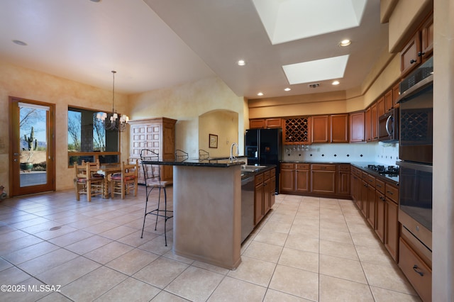 kitchen featuring a breakfast bar, light tile patterned floors, appliances with stainless steel finishes, brown cabinetry, and a notable chandelier