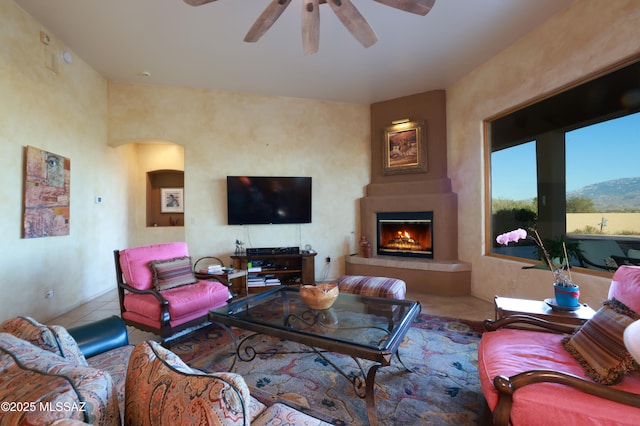 tiled living area featuring arched walkways, ceiling fan, and a fireplace