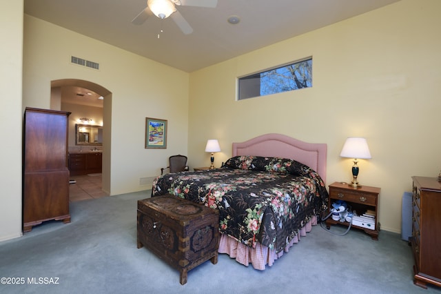 bedroom featuring visible vents, carpet flooring, arched walkways, ensuite bath, and a ceiling fan