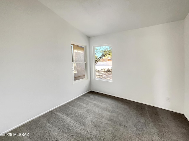 spare room with baseboards, dark carpet, and vaulted ceiling