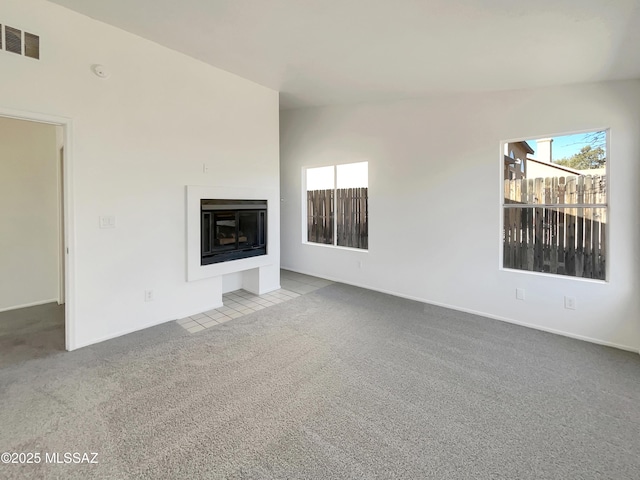 unfurnished living room featuring visible vents, a healthy amount of sunlight, carpet, and a glass covered fireplace