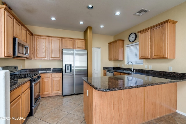 kitchen with visible vents, dark stone counters, appliances with stainless steel finishes, a peninsula, and a sink