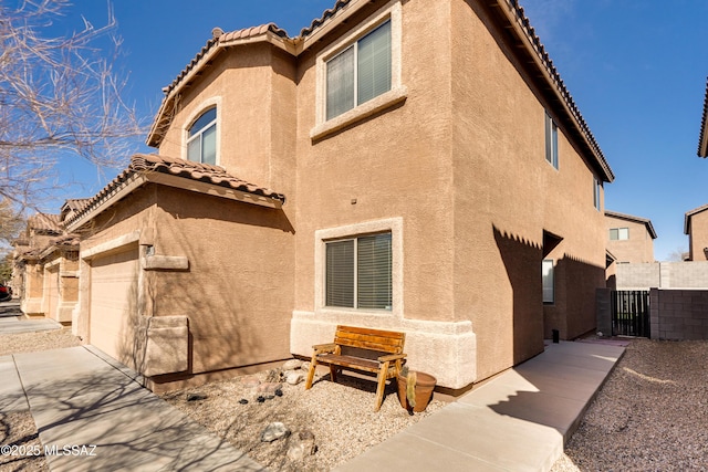 rear view of house featuring a tile roof, a garage, and stucco siding