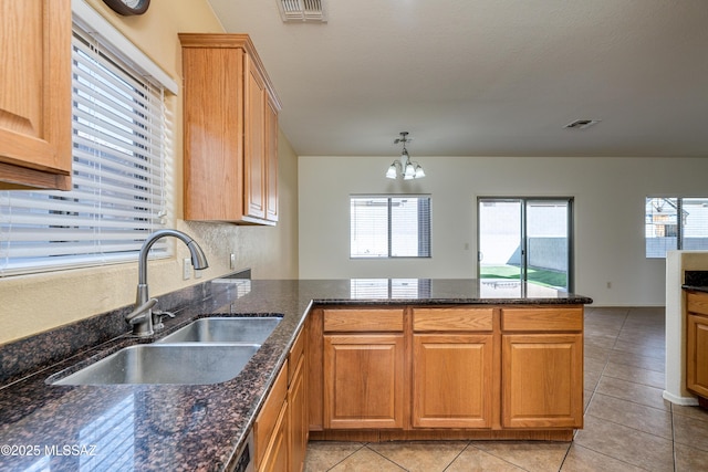 kitchen with visible vents, light tile patterned floors, a peninsula, a notable chandelier, and a sink