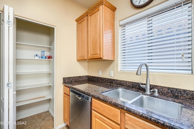 kitchen with light brown cabinetry, dishwasher, dark stone countertops, tile patterned floors, and a sink