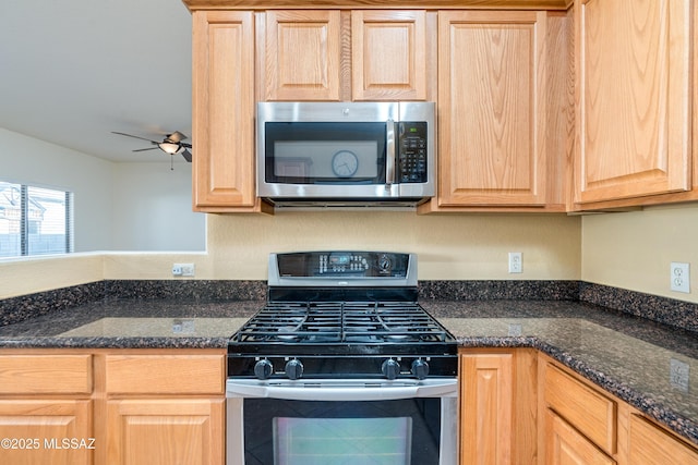 kitchen featuring light brown cabinetry, appliances with stainless steel finishes, dark stone counters, and a ceiling fan