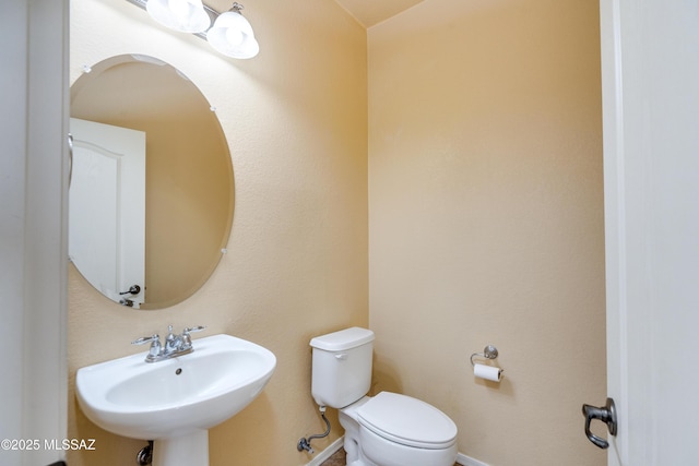 half bathroom with toilet, baseboards, and a sink