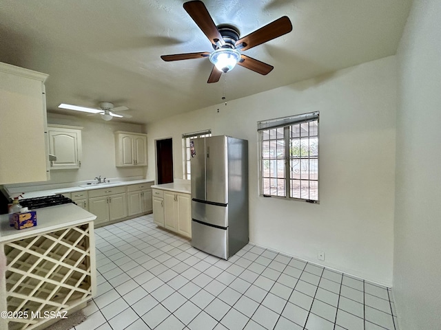 kitchen with a ceiling fan, a sink, freestanding refrigerator, light countertops, and light tile patterned floors