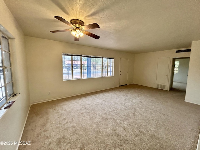 carpeted empty room with baseboards, visible vents, a textured ceiling, and a ceiling fan