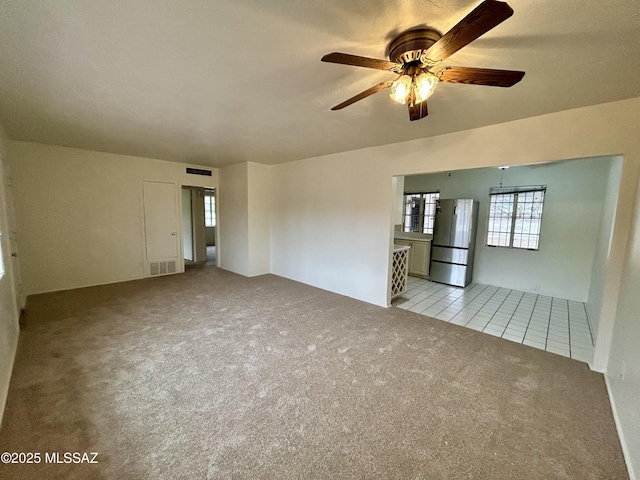 tiled empty room with visible vents, carpet floors, and ceiling fan