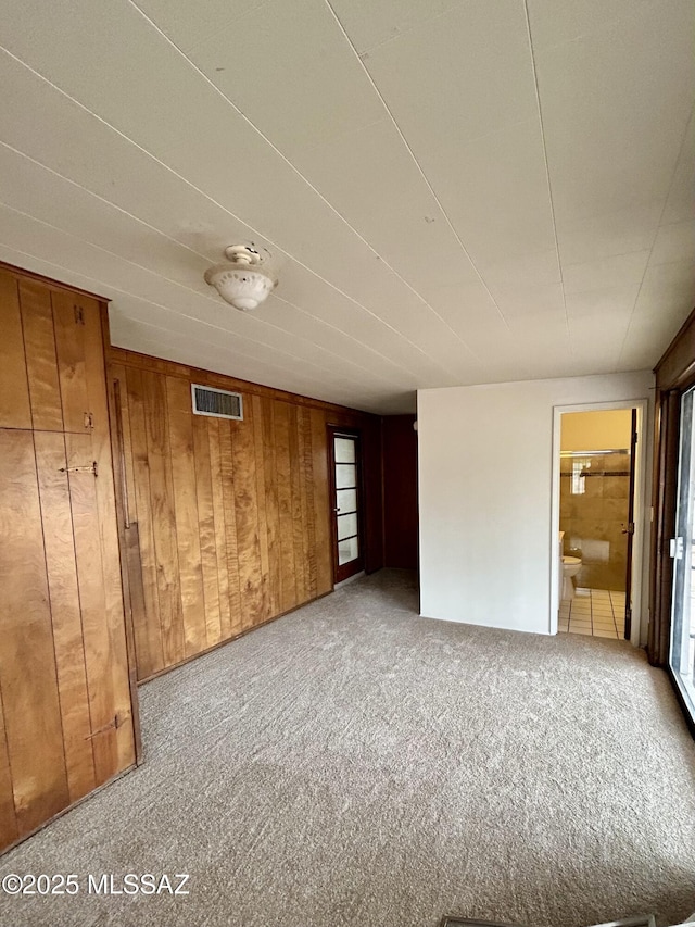 carpeted spare room featuring visible vents and wood walls