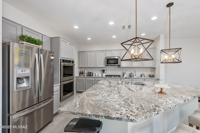 kitchen with visible vents, gray cabinets, tasteful backsplash, stainless steel appliances, and a breakfast bar area