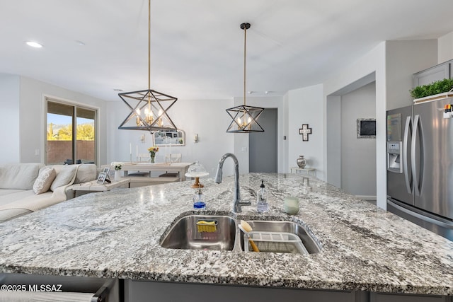 kitchen with light stone counters, a center island with sink, stainless steel fridge with ice dispenser, a sink, and open floor plan