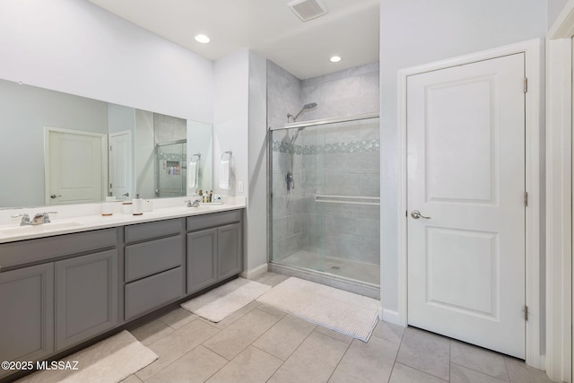 bathroom with visible vents, double vanity, a sink, a shower stall, and tile patterned floors