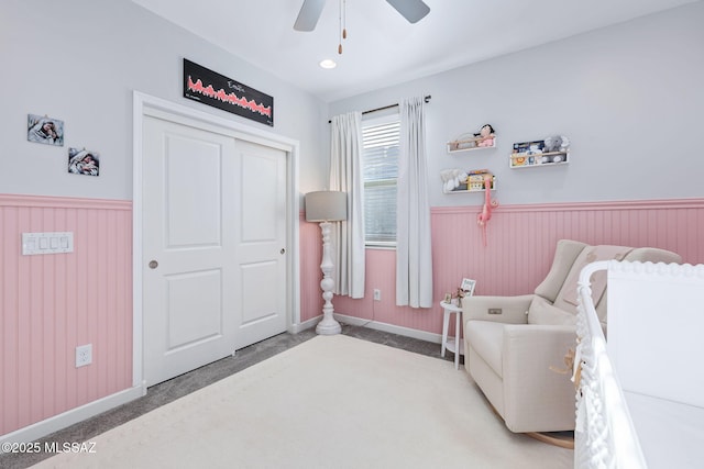 bedroom with a closet, a wainscoted wall, light colored carpet, and a ceiling fan