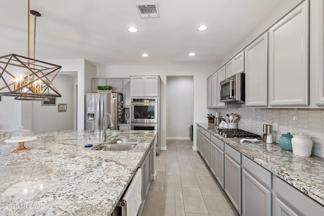 kitchen featuring visible vents, light stone counters, decorative backsplash, stainless steel appliances, and a sink