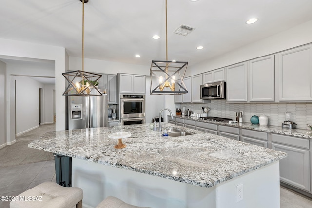 kitchen with visible vents, a sink, a kitchen breakfast bar, tasteful backsplash, and appliances with stainless steel finishes