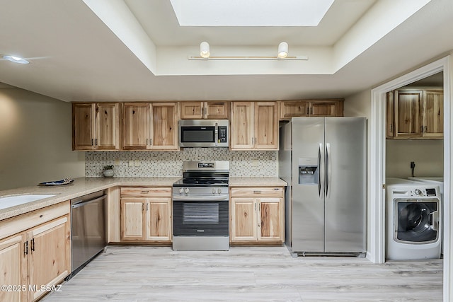 kitchen featuring washer / clothes dryer, a raised ceiling, a skylight, and appliances with stainless steel finishes