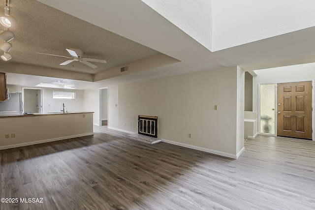 unfurnished living room with baseboards, wood finished floors, a ceiling fan, a sink, and a tray ceiling