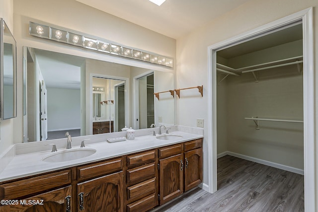 bathroom featuring a sink, wood finished floors, a walk in closet, baseboards, and double vanity