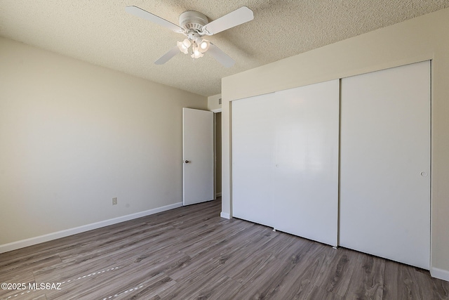 unfurnished bedroom featuring a closet, a textured ceiling, baseboards, wood finished floors, and a ceiling fan