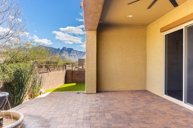 view of patio with a mountain view, a ceiling fan, and fence