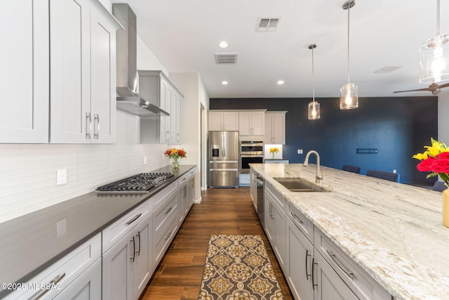 kitchen with a sink, wall chimney exhaust hood, stainless steel appliances, tasteful backsplash, and visible vents