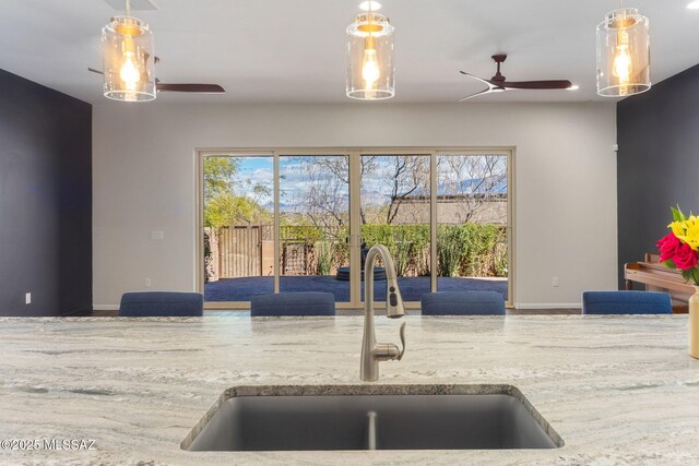 kitchen featuring a sink, light stone counters, baseboards, and a ceiling fan