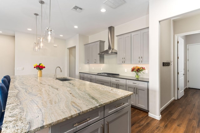 kitchen with wall chimney range hood, gray cabinetry, a sink, and visible vents