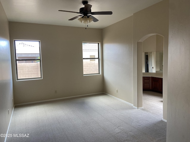 spare room featuring arched walkways, light colored carpet, baseboards, and a ceiling fan