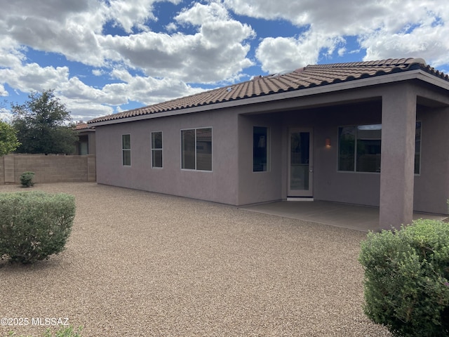 rear view of house featuring a tile roof, stucco siding, fence, and a patio area