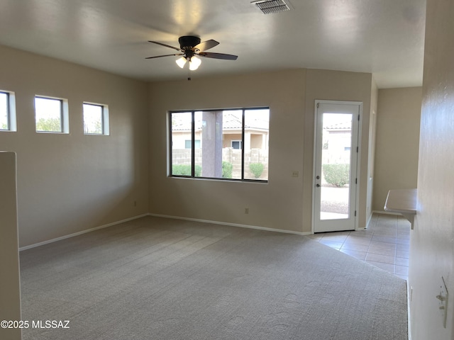 interior space with visible vents, baseboards, ceiling fan, light colored carpet, and light tile patterned floors