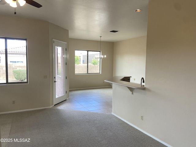 interior space with baseboards, light carpet, and ceiling fan with notable chandelier