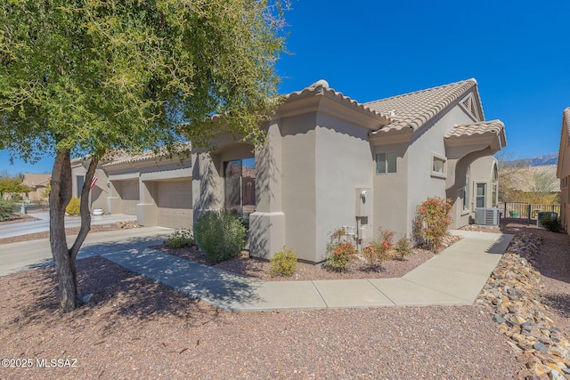 view of front of home featuring concrete driveway, a tiled roof, central AC unit, and stucco siding