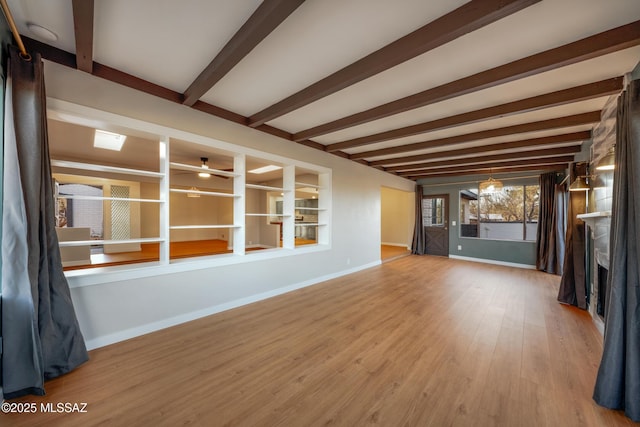 unfurnished living room featuring beam ceiling, wood finished floors, a fireplace, baseboards, and ceiling fan