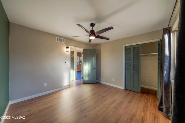 unfurnished bedroom featuring visible vents, baseboards, a closet, and wood finished floors