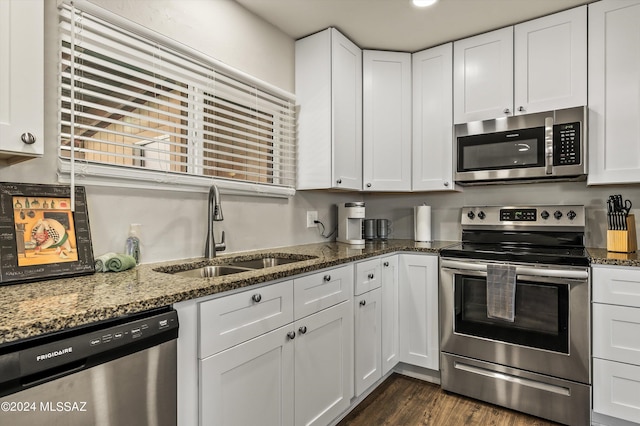 kitchen with dark stone counters, dark wood-style floors, white cabinets, stainless steel appliances, and a sink