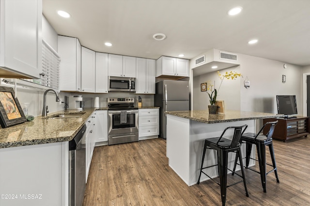 kitchen with dark wood-style floors, a breakfast bar, a sink, appliances with stainless steel finishes, and white cabinetry