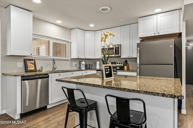 kitchen with a breakfast bar, dark wood finished floors, a sink, stainless steel appliances, and white cabinets