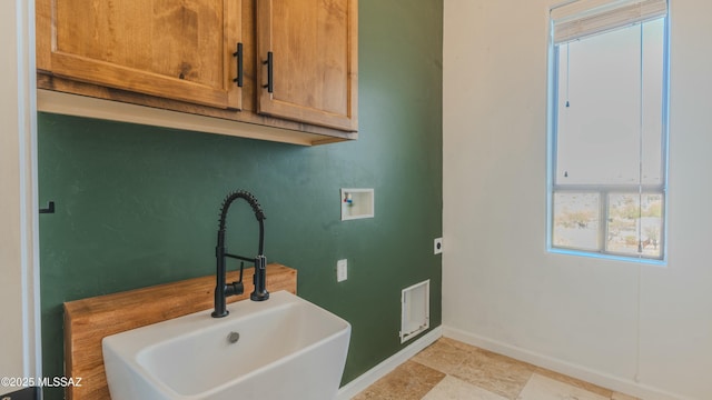 clothes washing area with a sink, cabinet space, baseboards, and washer hookup