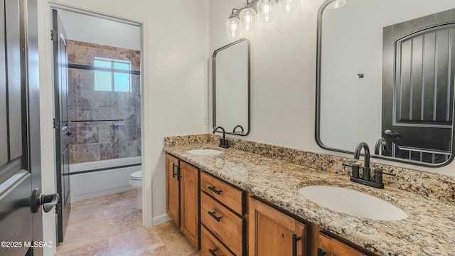 bathroom featuring a sink, combined bath / shower with glass door, toilet, and double vanity